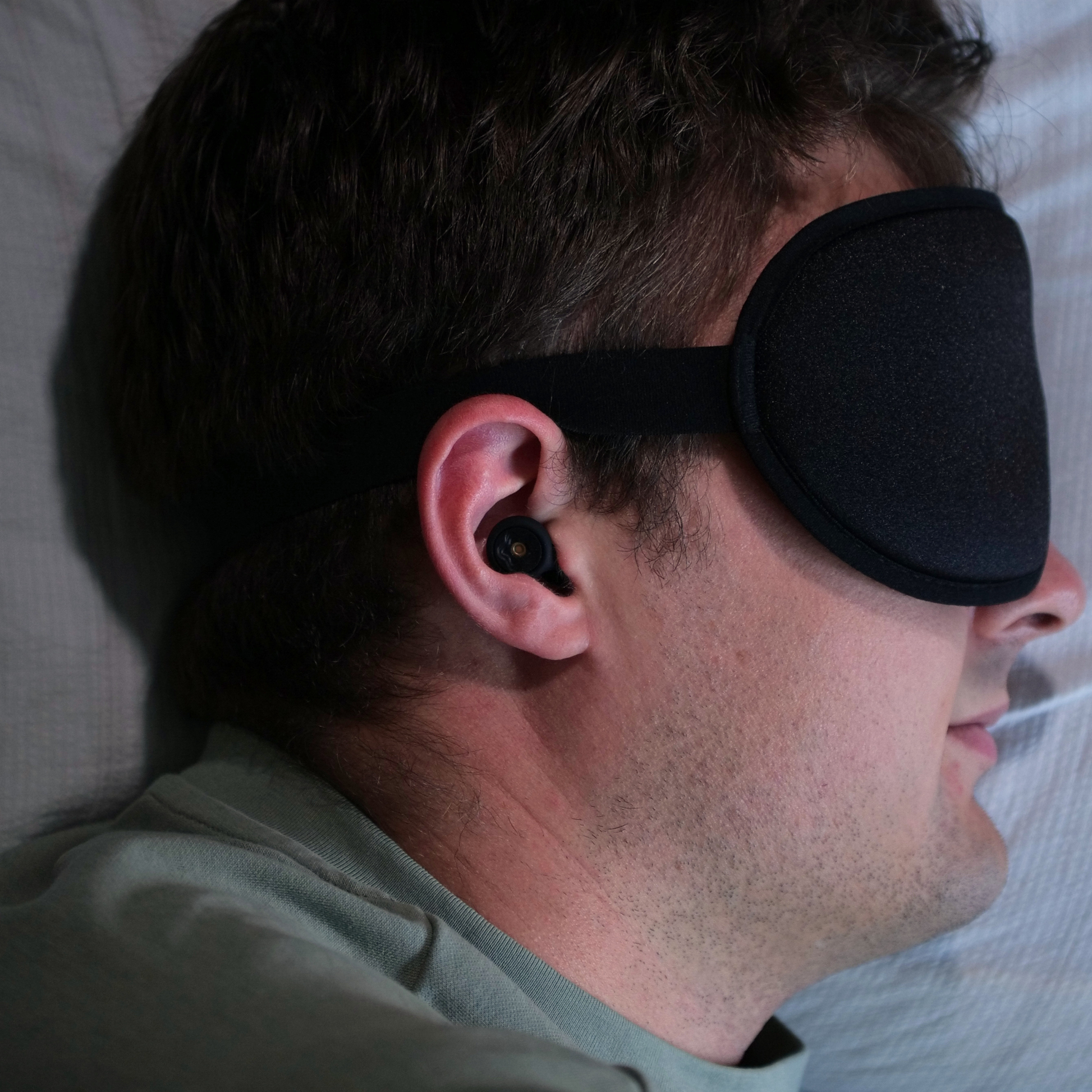A male side sleeper wearing Infinity Sleep 3D graphene sleep mask and silicone earplugs.