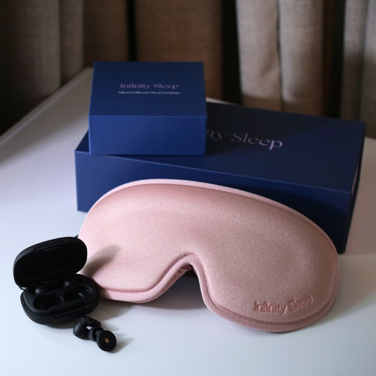 Pink sleep mask with black earplugs on a white surface, branded 'Infinity Sleep'.